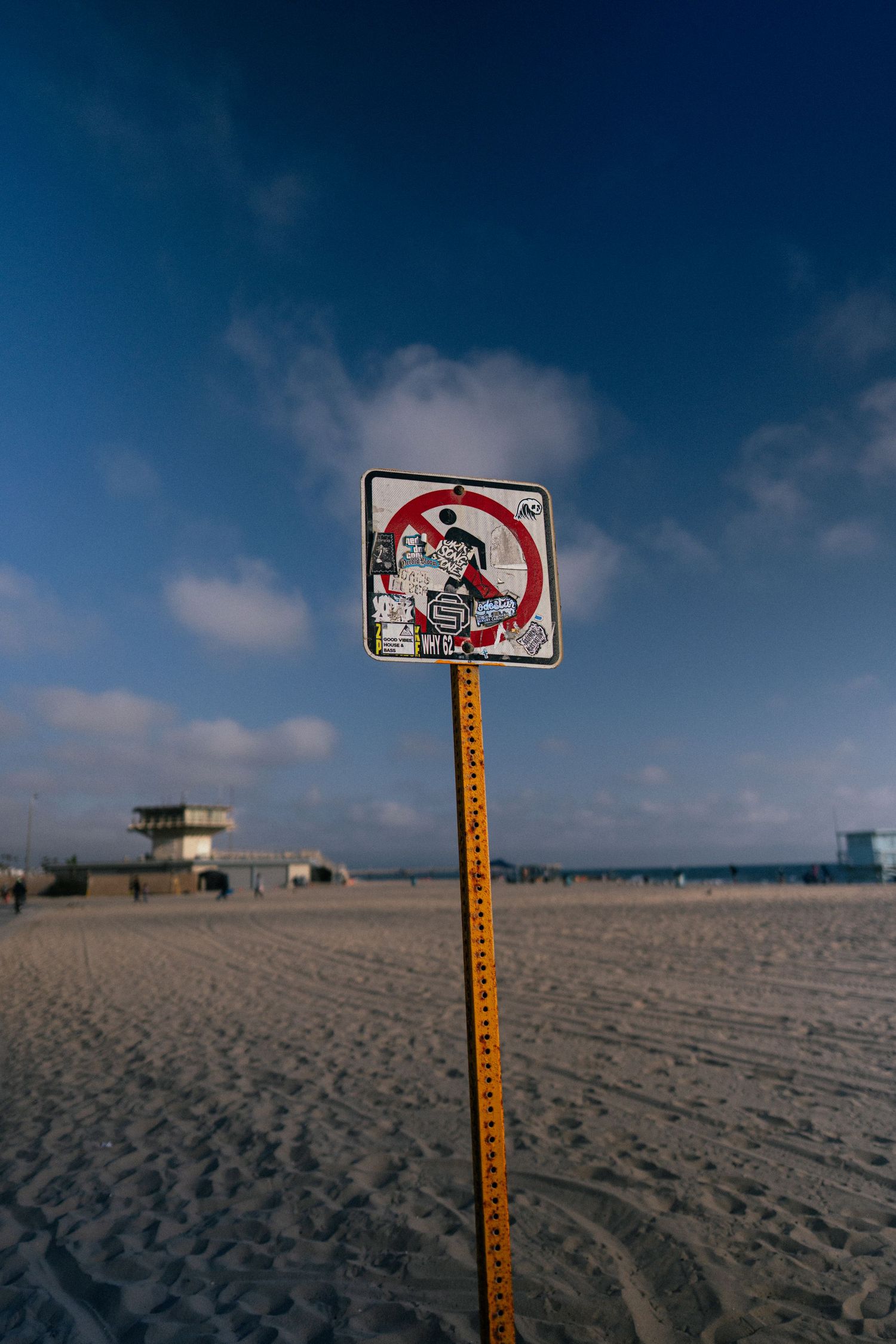 No swimming sign on a pole at a beach with stickers on it