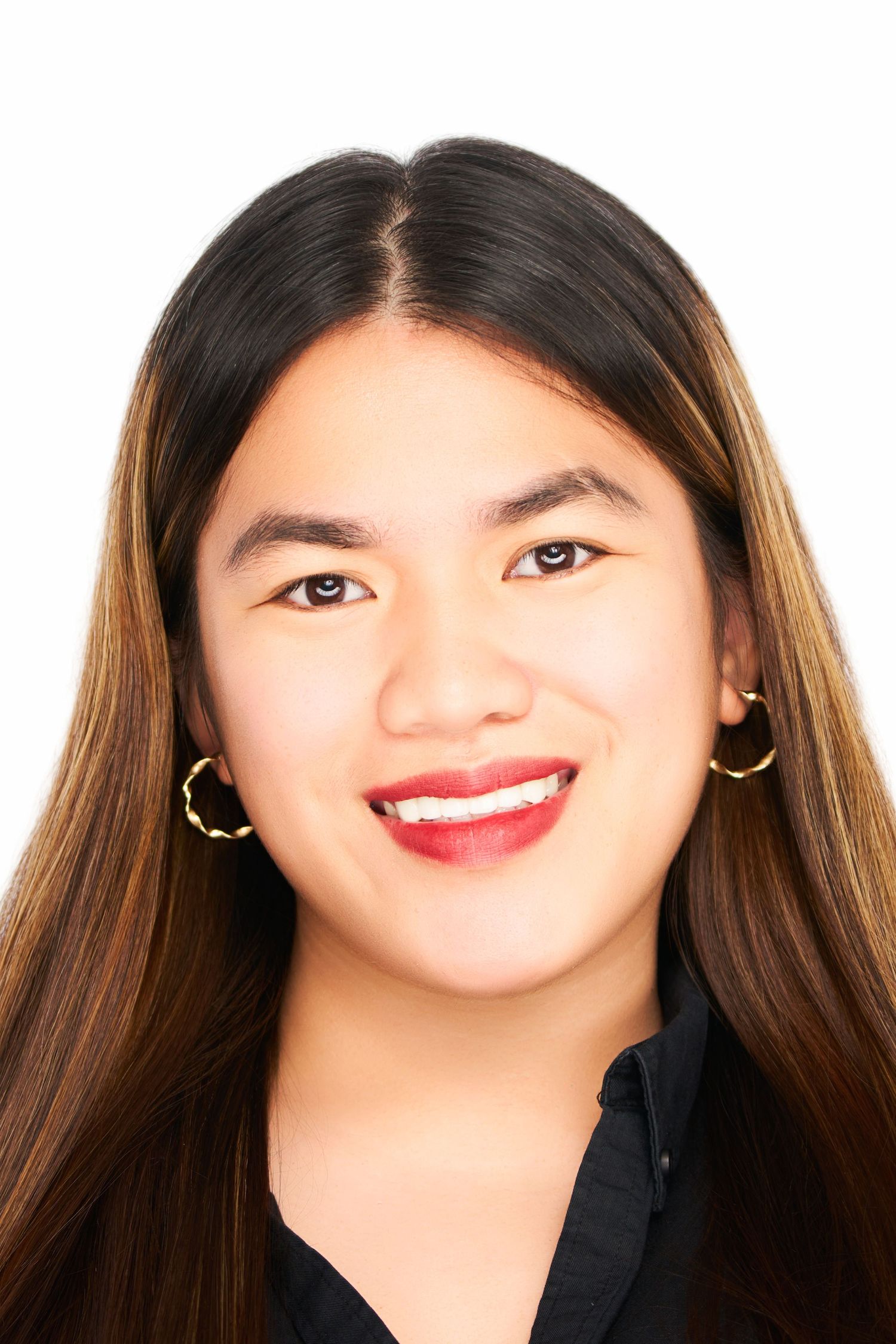 Young Asian woman smiling with red lipstick, gold hoop earrings, and long dark hair on white background.