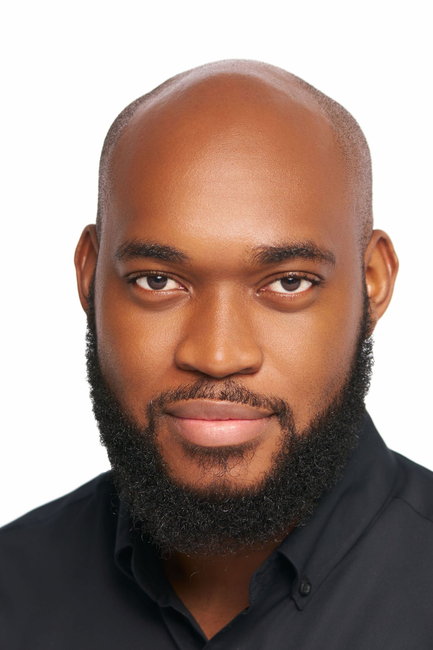 Close-up portrait of a bald Black man with a full beard wearing a black shirt against white background.
