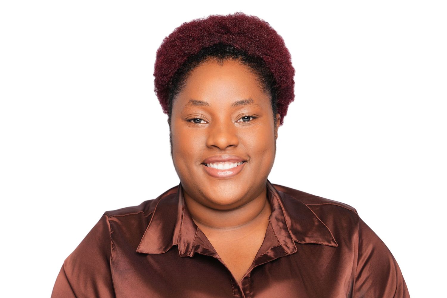 Smiling woman with natural dark red hair wearing a brown satin blouse against a white background.