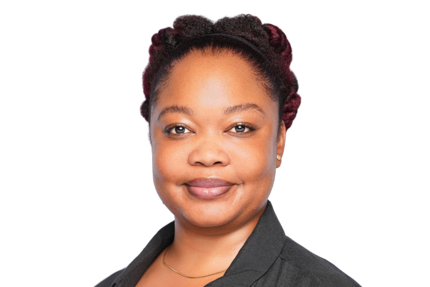 Professional headshot of a smiling woman with braided hairstyle wearing a dark blazer against white background.