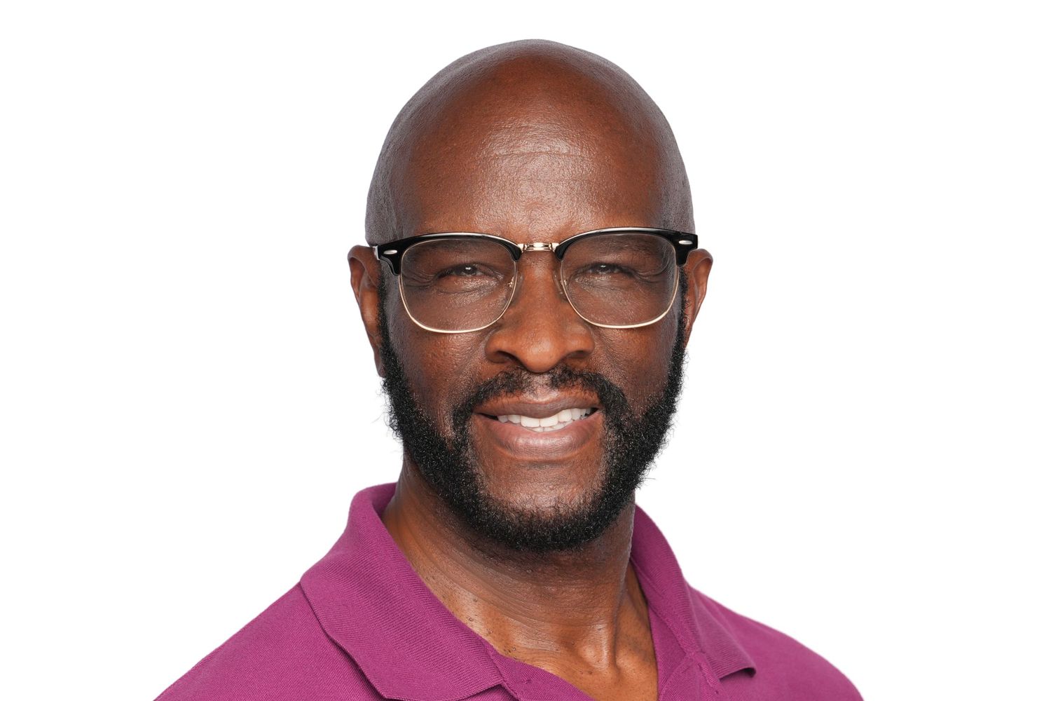 Smiling bald black man with glasses and a beard wearing a magenta polo shirt against a white background.
