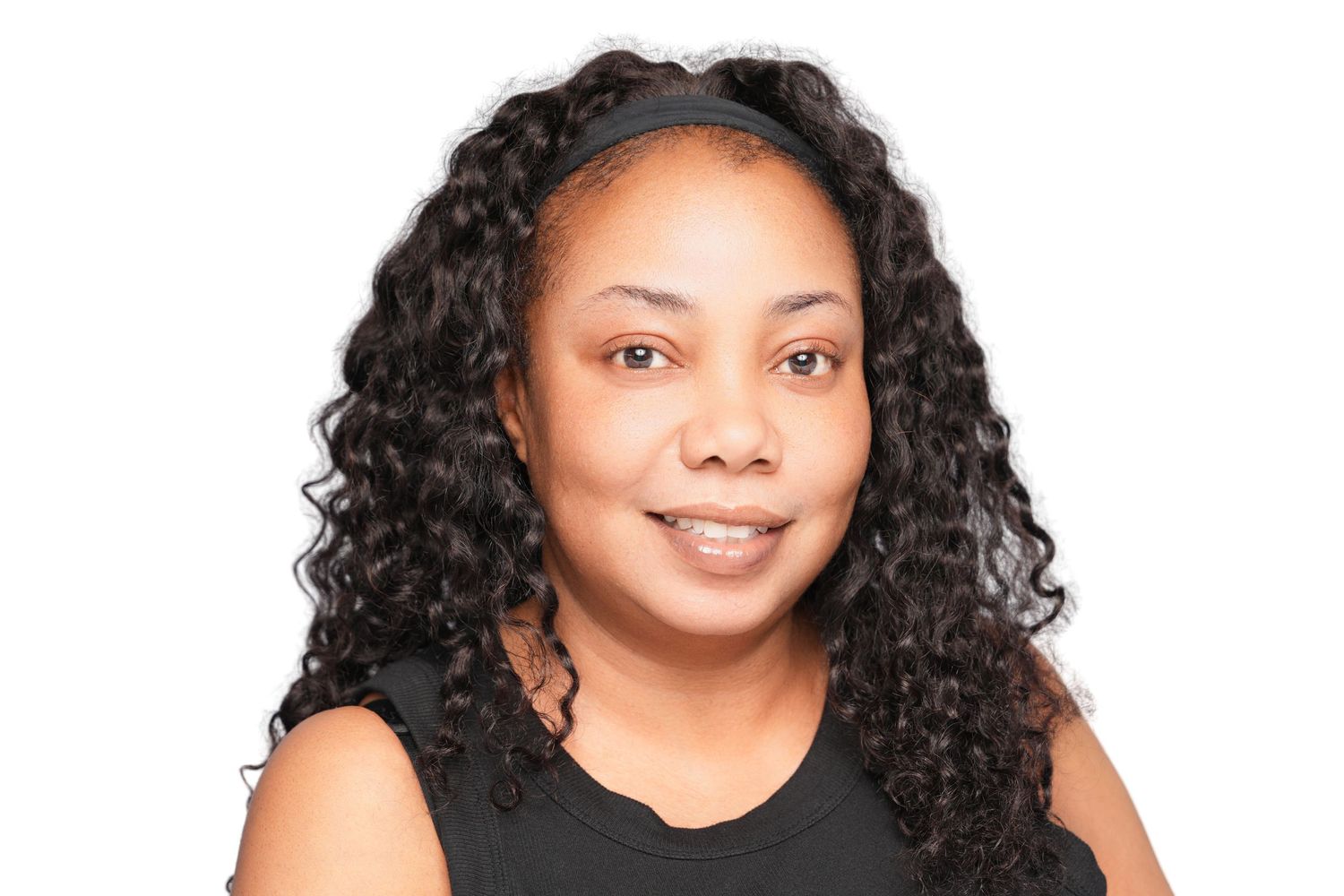 Professional headshot of a smiling woman with long curly black hair wearing a black sleeveless top on white background.