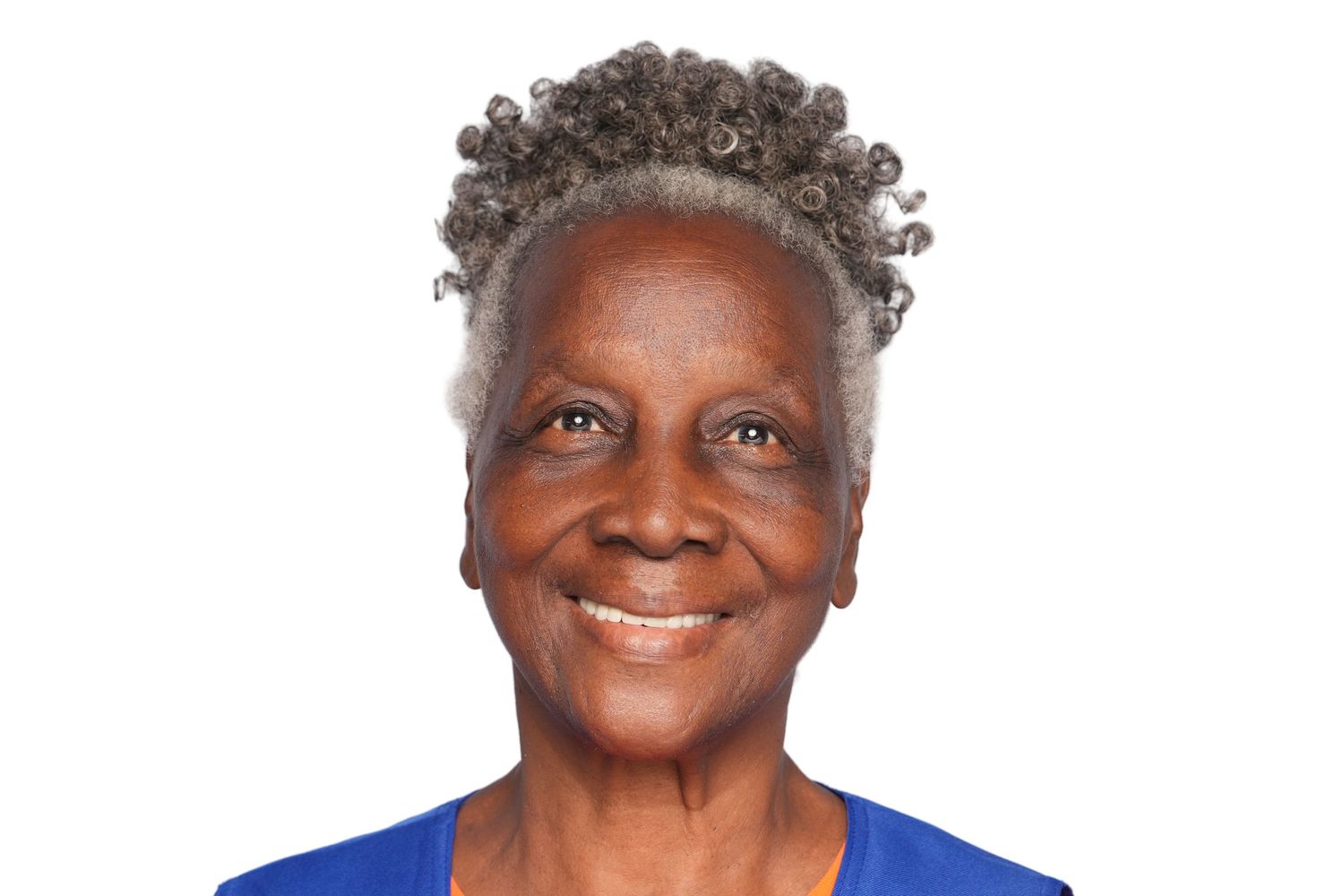 Smiling elderly black woman with gray curly hair wearing a blue top against a white background.