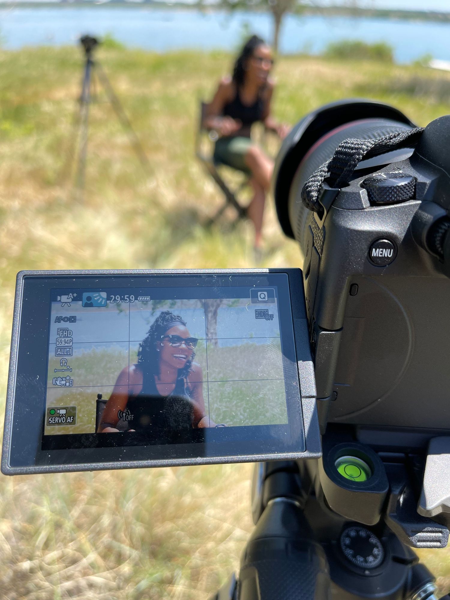 Camera LCD screen showing a woman being interviewed outdoors near a waterfront on a sunny day.