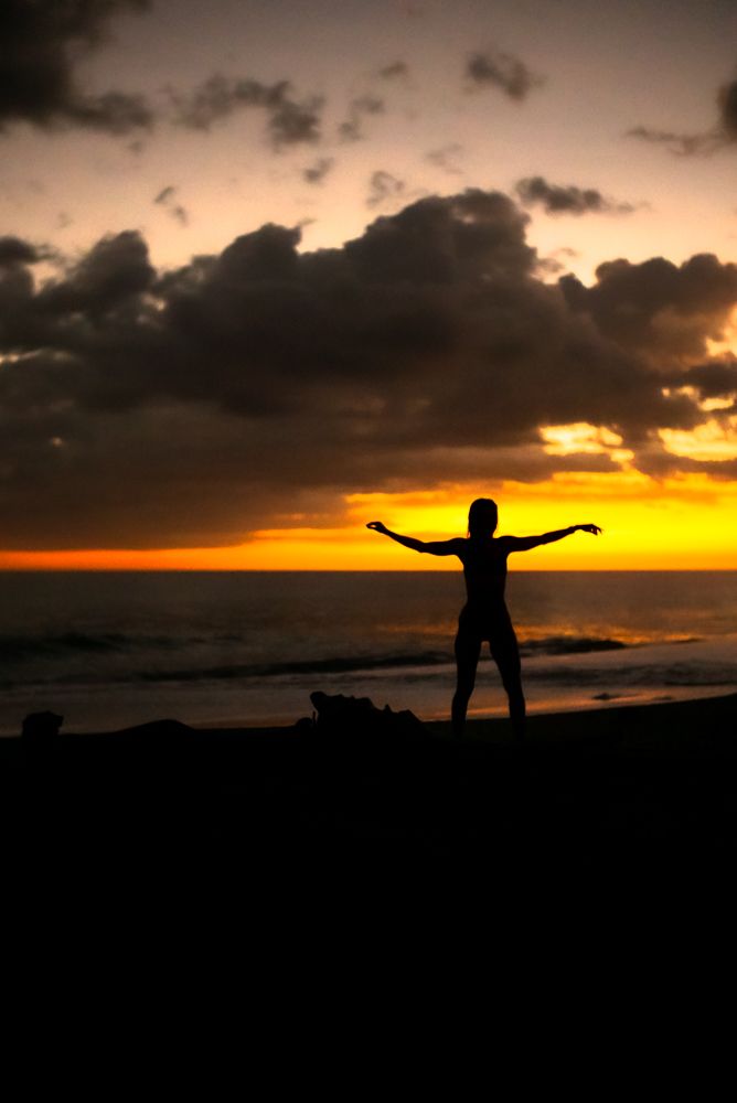 Silhouette of a person with arms outstretched standing on a beach at a dramatic golden sunset.