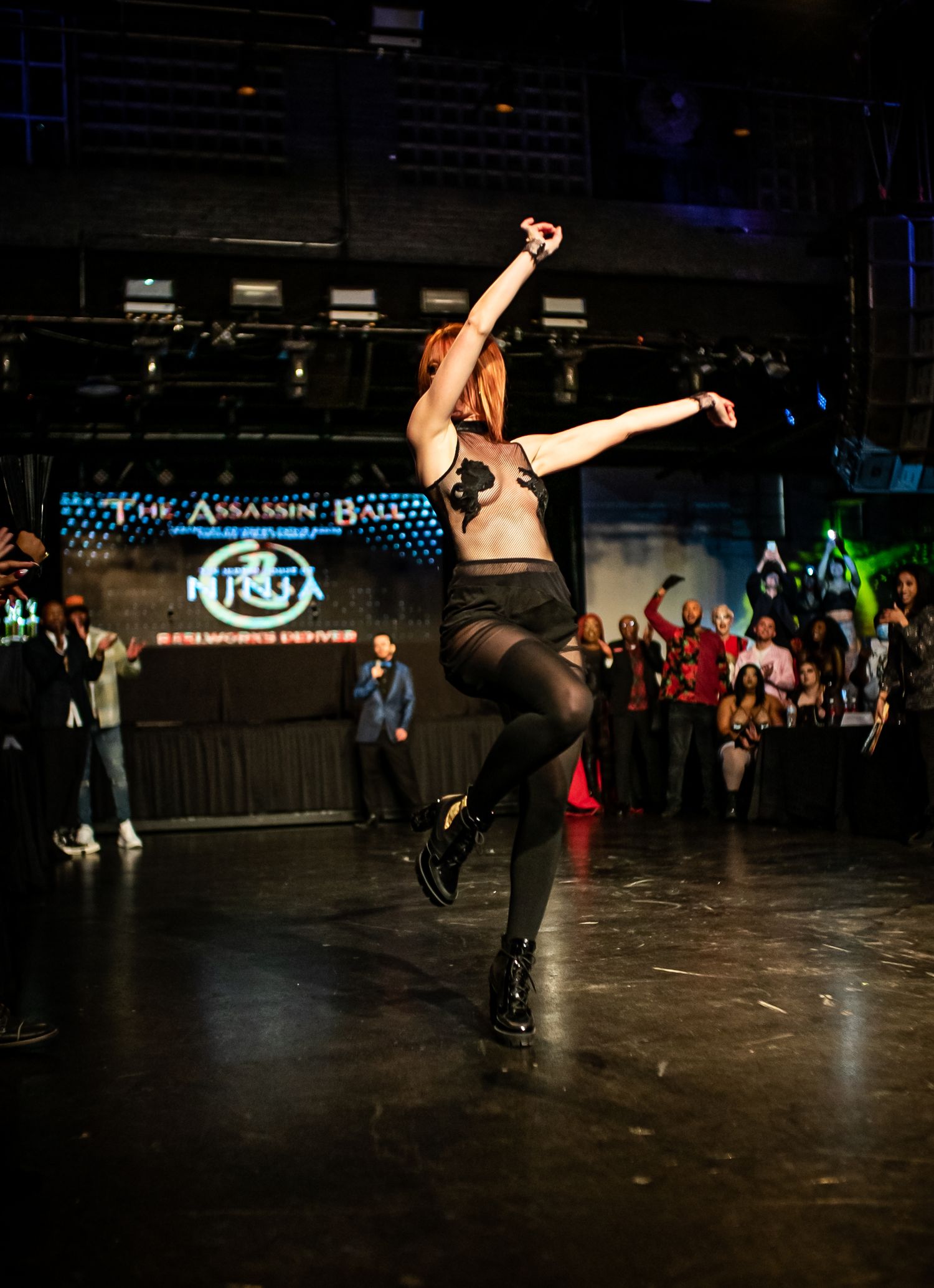 Red-haired dancer leaping on stage at The Assassin Ball NRG event in Denver.