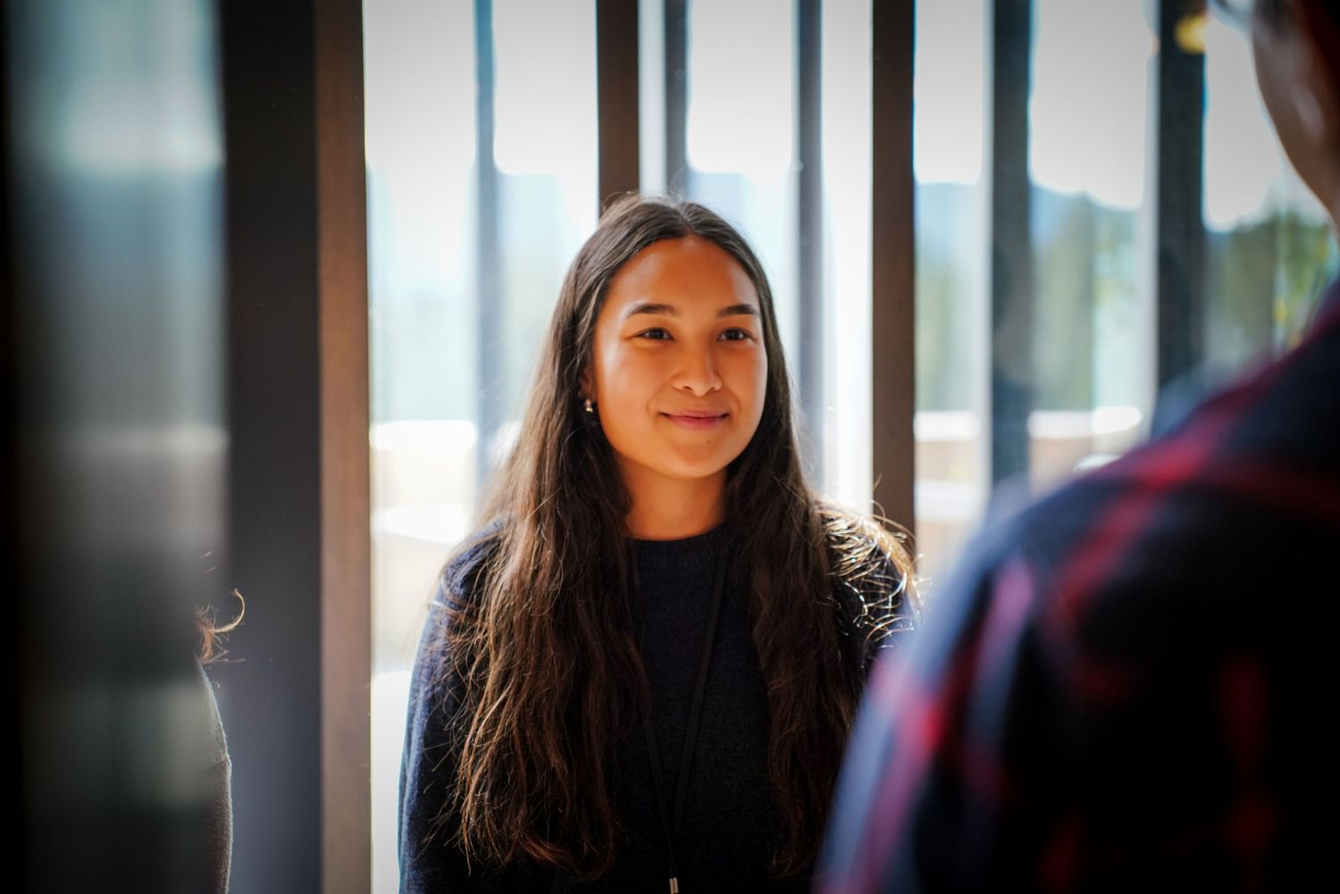 Young woman with long dark hair smiling softly in natural window light.