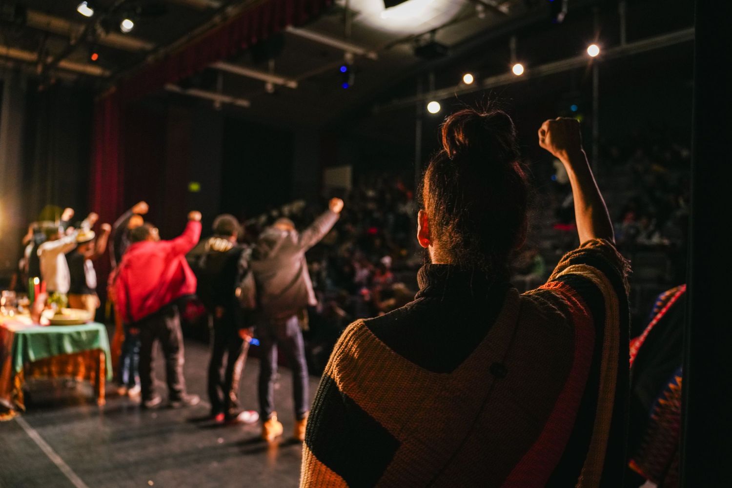 Audience members raise fists in solidarity at a live cultural performance on a theater stage.