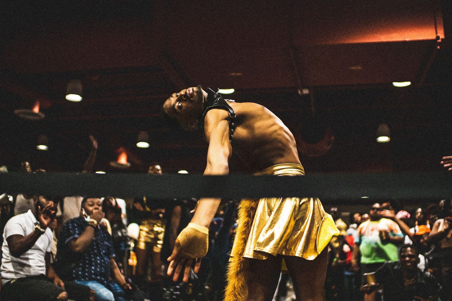 Muscular performer in gold shorts bows on stage before large crowd at energetic live event.