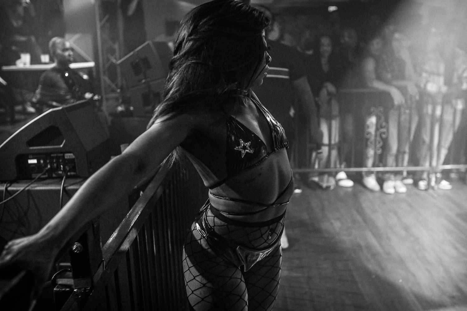 Black and white photo of a woman in fishnet and star-print outfit performing on a dimly lit stage.