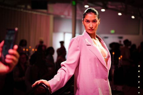Model walks runway in oversized pink blazer suit at a contemporary fashion show event.
