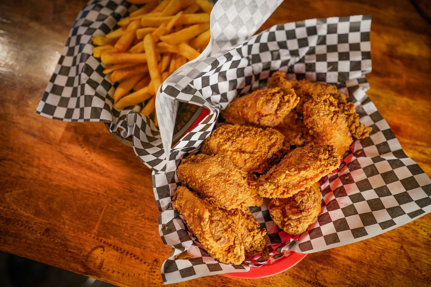 Golden fried chicken pieces and french fries served in red baskets lined with checkered paper.