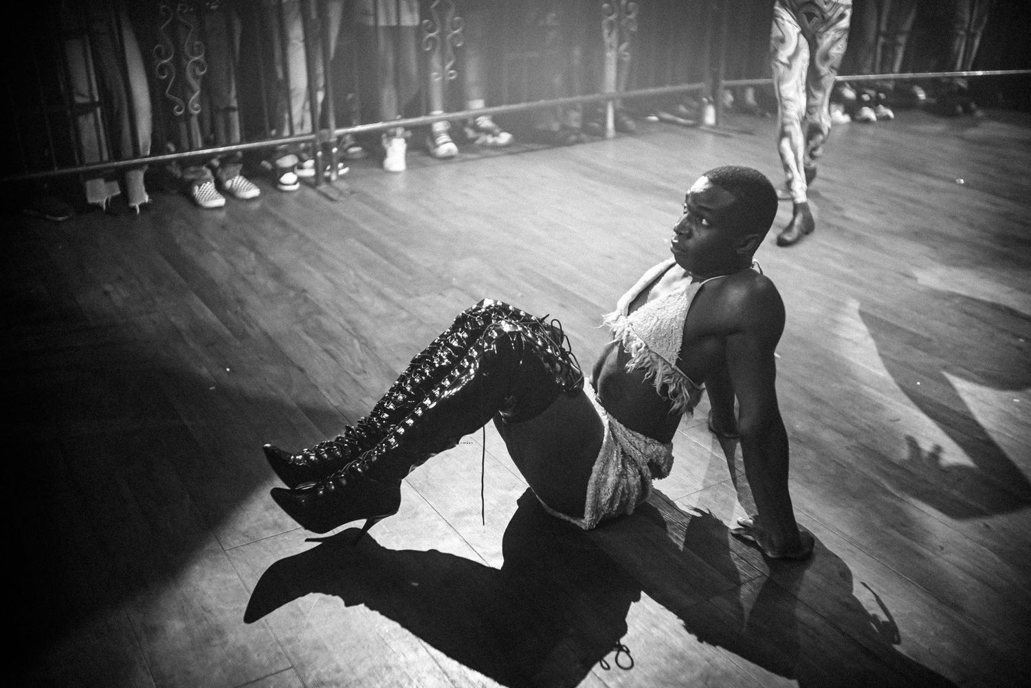 Black and white photo of dancer in thigh-high boots performing floor routine on stage.