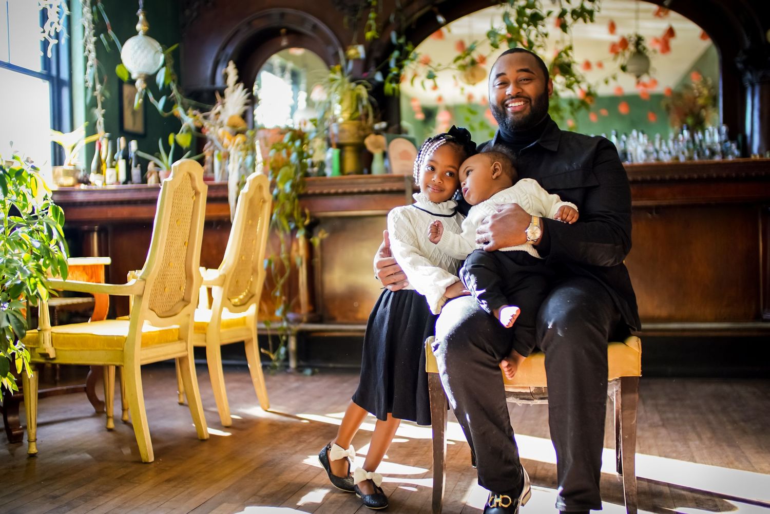Smiling father sitting with two young children in decorated indoor setting.