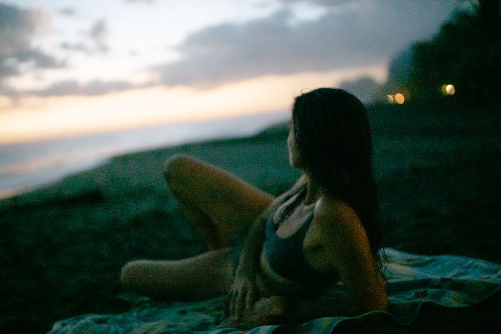 Young woman relaxes on a blanket at the beach during a peaceful twilight evening by the ocean.