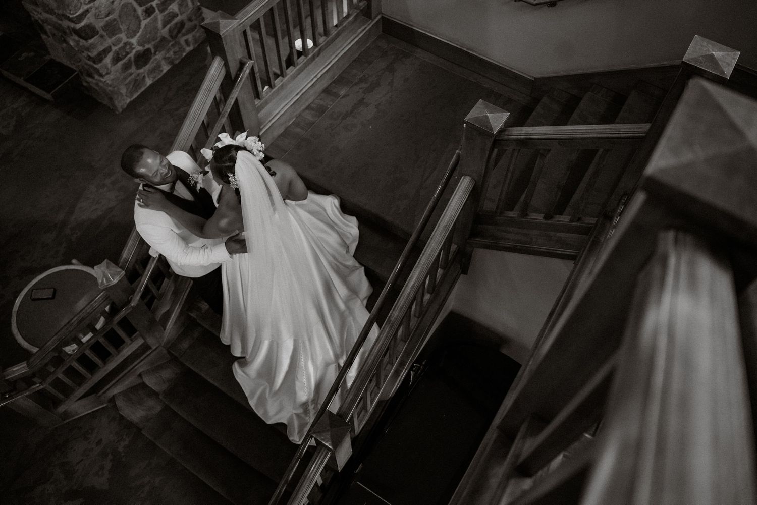 Black and white photo of a bride and groom sharing a romantic moment on wooden staircase at their wedding venue.
