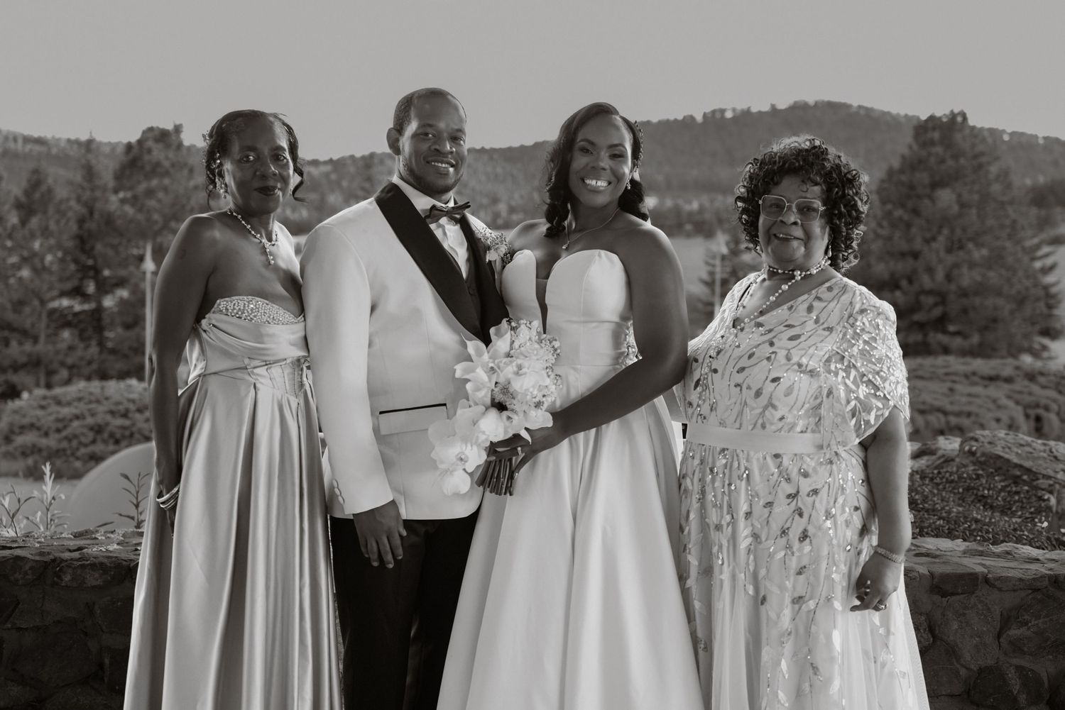 Black and white wedding photo of a bride, groom, and two women posing outdoors with scenic hills in the background.