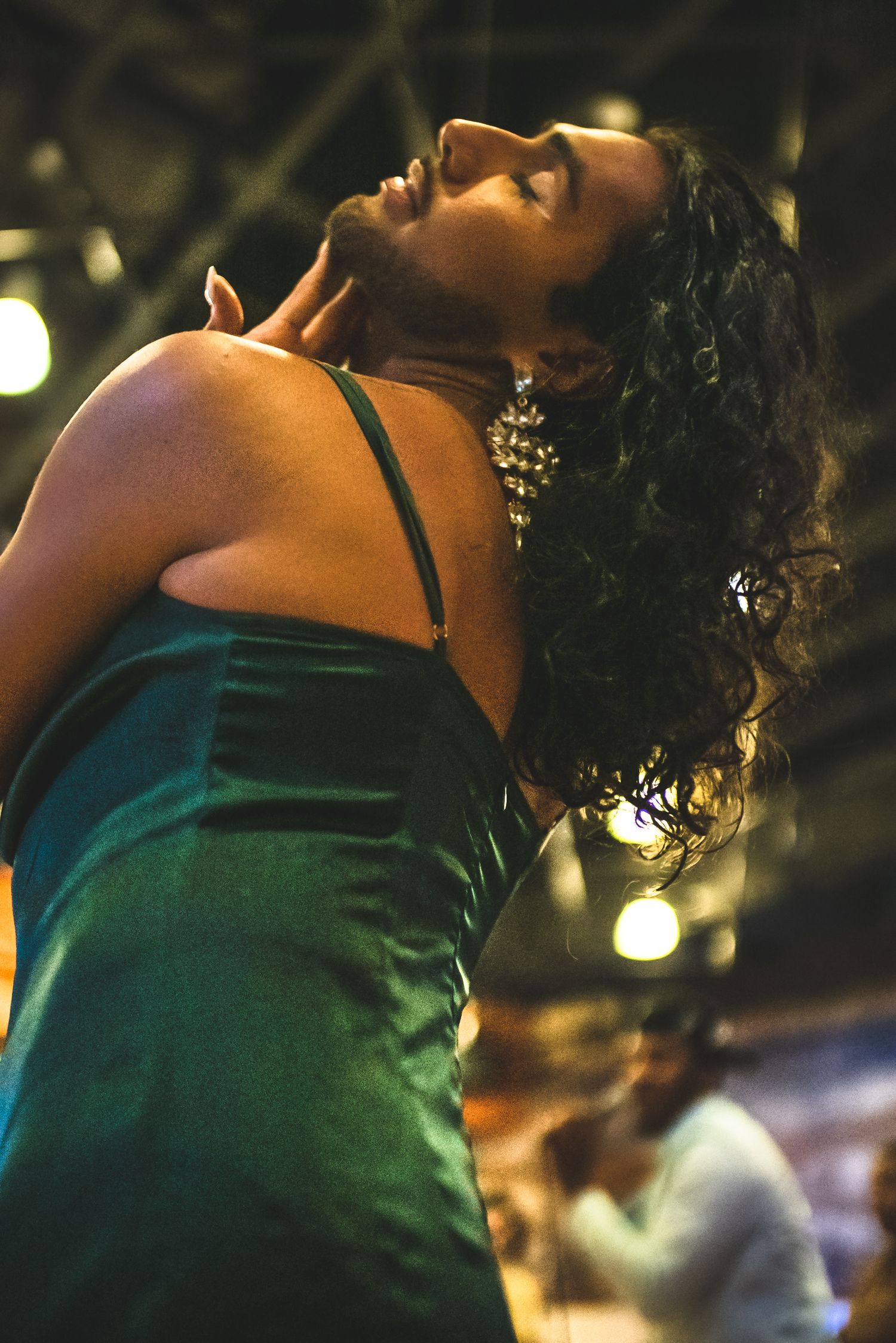Woman in green satin dress dancing with head tilted back under warm stage lights.