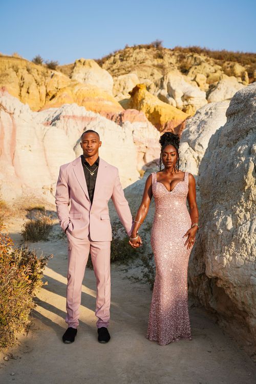 Couple in matching pink outfits holding hands in colorful desert landscape.