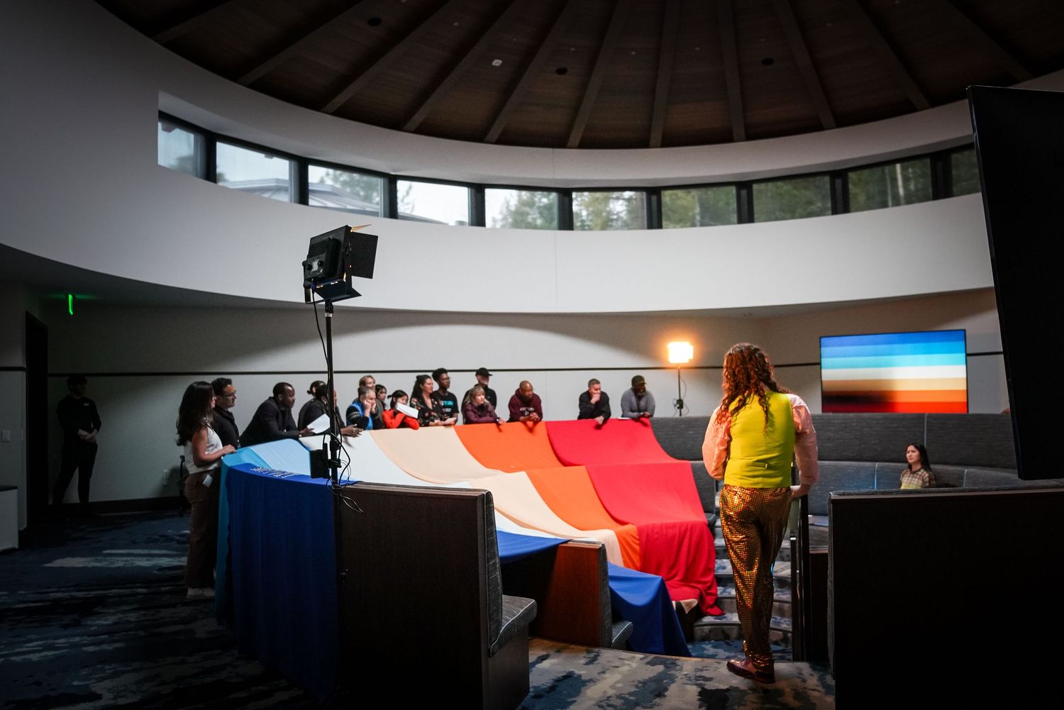 Group gathered in circular room with colorful fabric display and presentation setup.