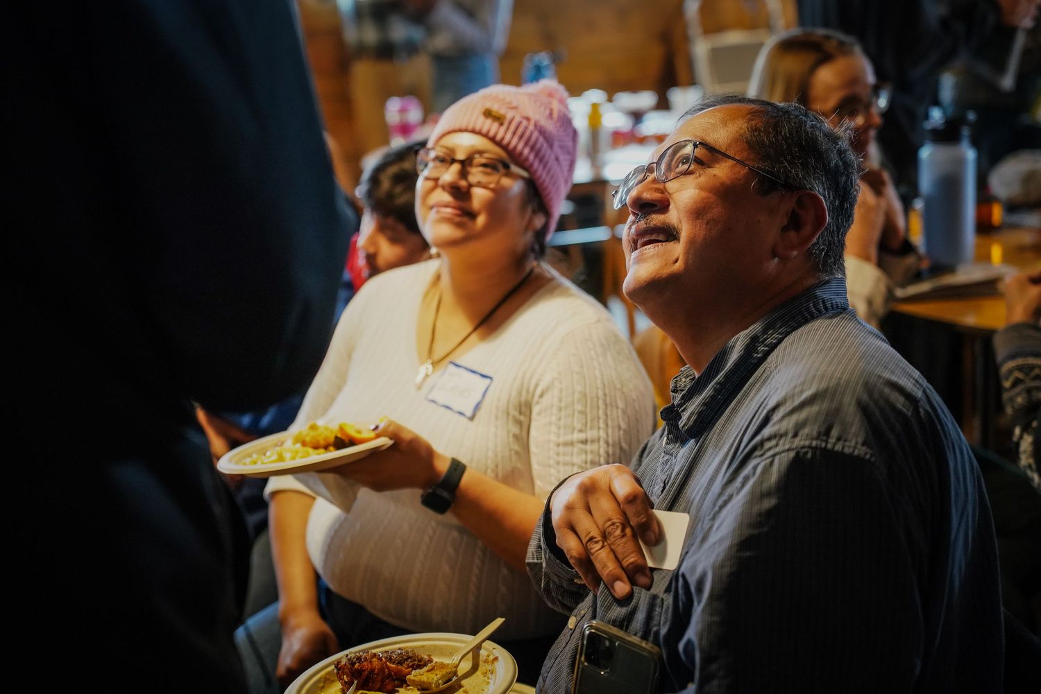 Happy man and woman laugh together while holding plates at a casual community dining event.