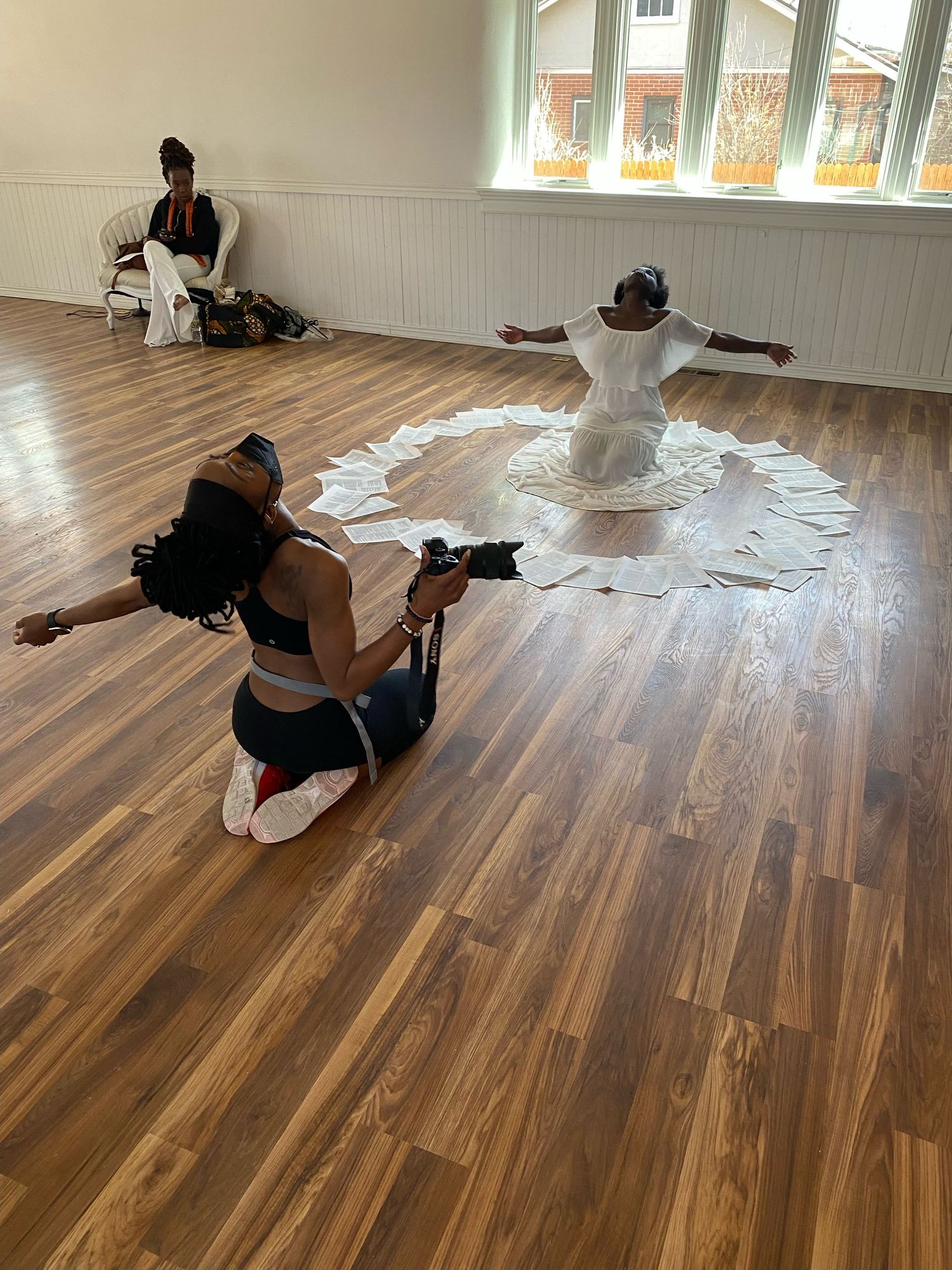 Photographer capturing a dancer performing in a circle of white paper on a hardwood floor in a bright studio.