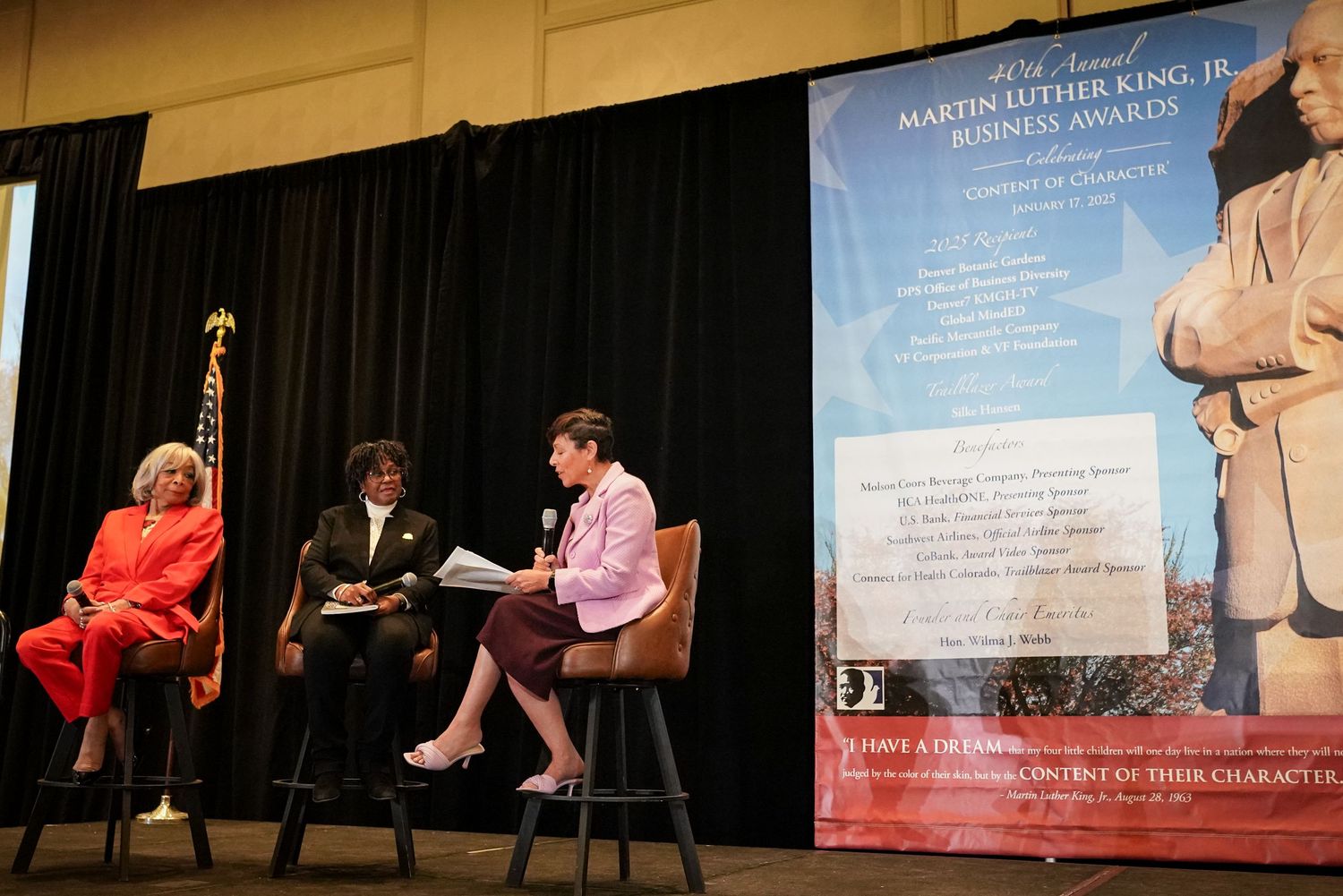 Panel discussion at Martin Luther King Jr. Business Awards ceremony with three speakers on decorated stage.