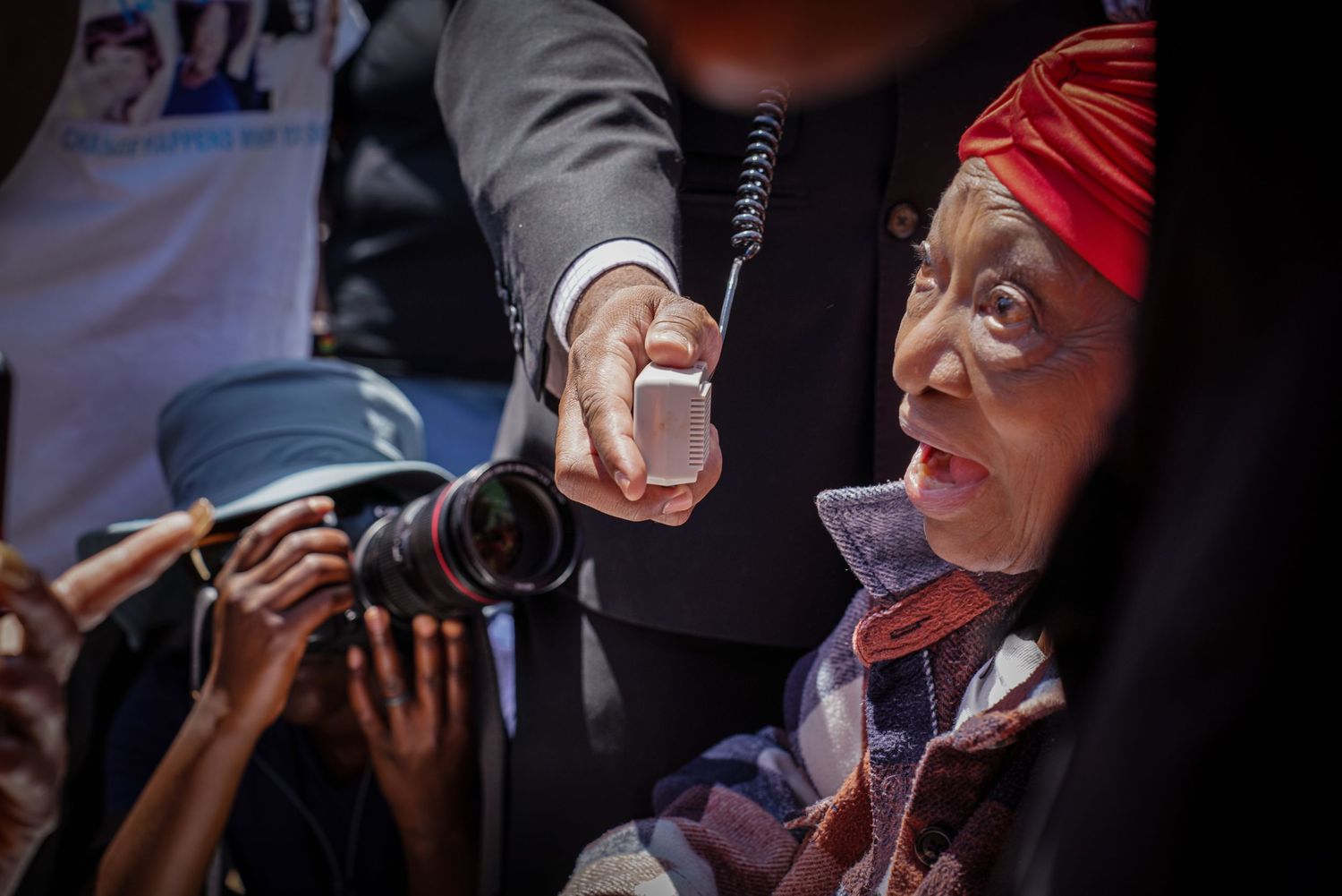 Elderly woman in red headwrap speaks into microphone at outdoor civil rights rally event.