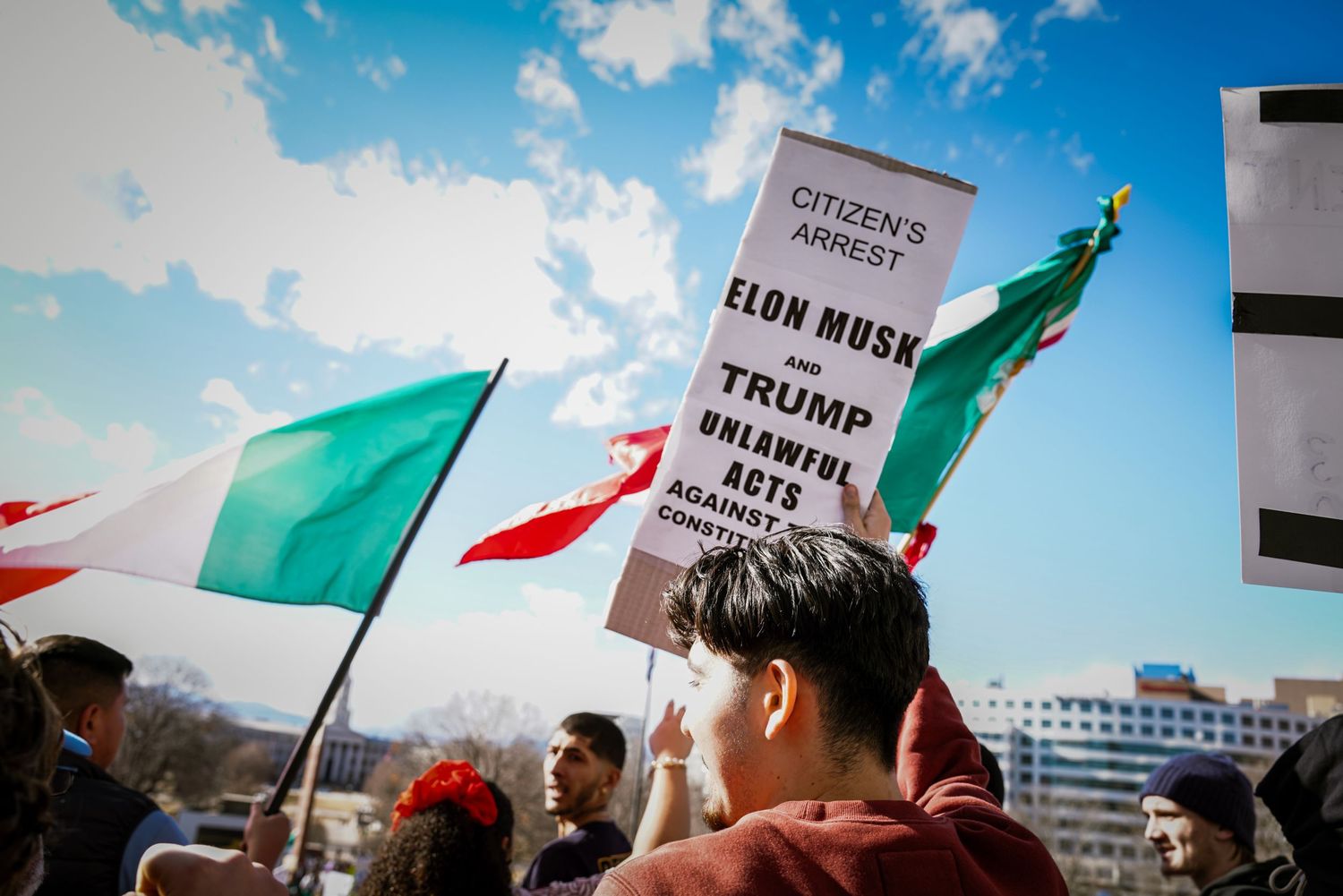 Protesters at a political rally holding a sign calling for citizen's arrest of Elon Musk and Trump for unlawful acts.