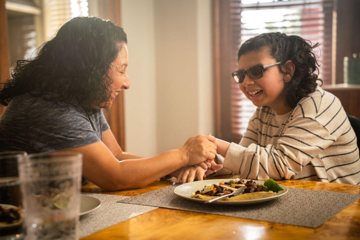 Mother and child with glasses laughing together over a meal at home dining table.