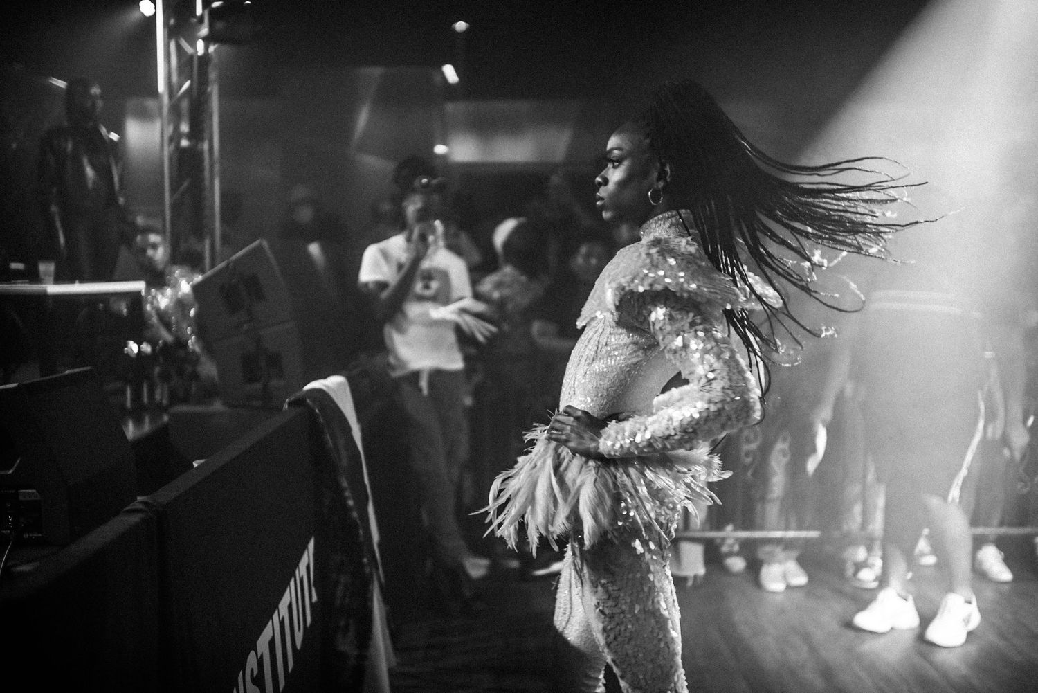Black and white photo of a woman in sequined outfit dancing with hair flowing at a nightclub event.