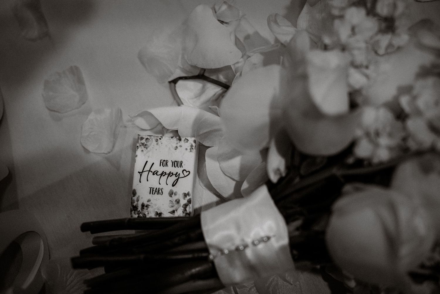 Black and white photo of a small Happy Places candle surrounded by white roses and flowers.