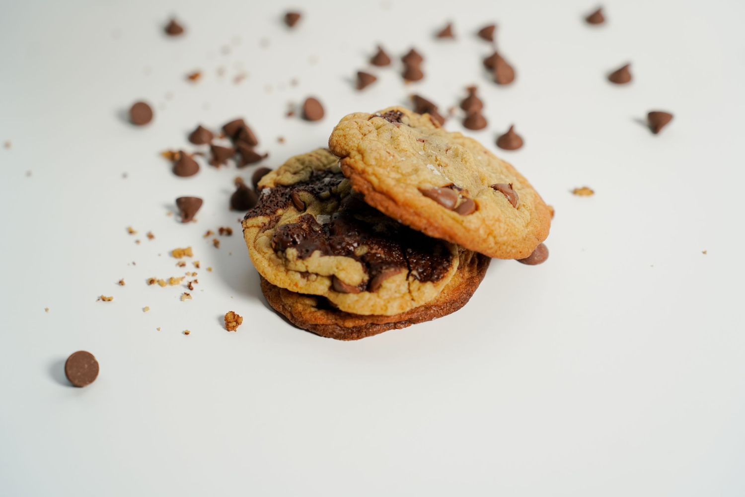 Two chocolate chip cookies stacked together with scattered chocolate chips on a white background.