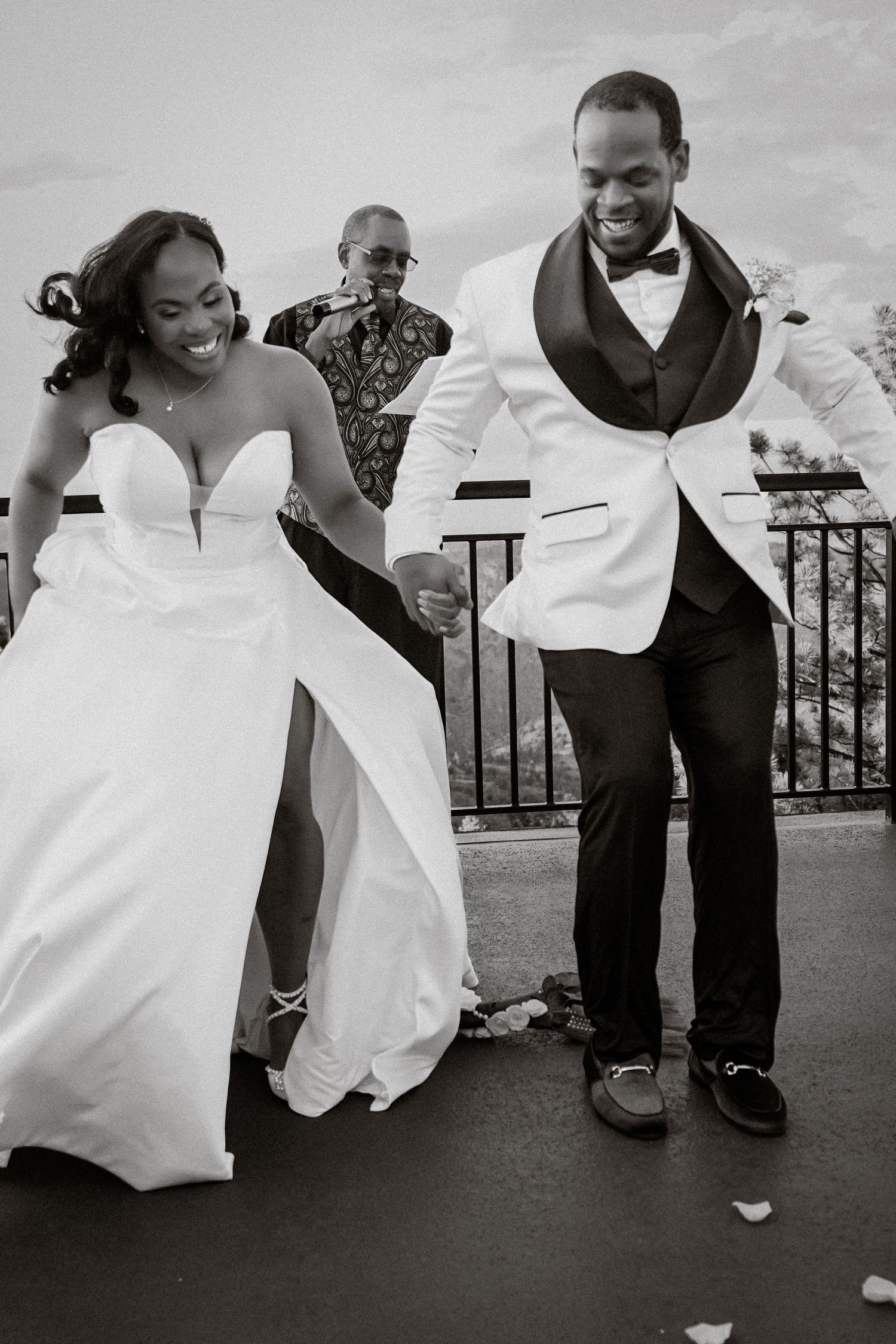Black and white photo of a joyful bride and groom holding hands at their outdoor wedding ceremony.