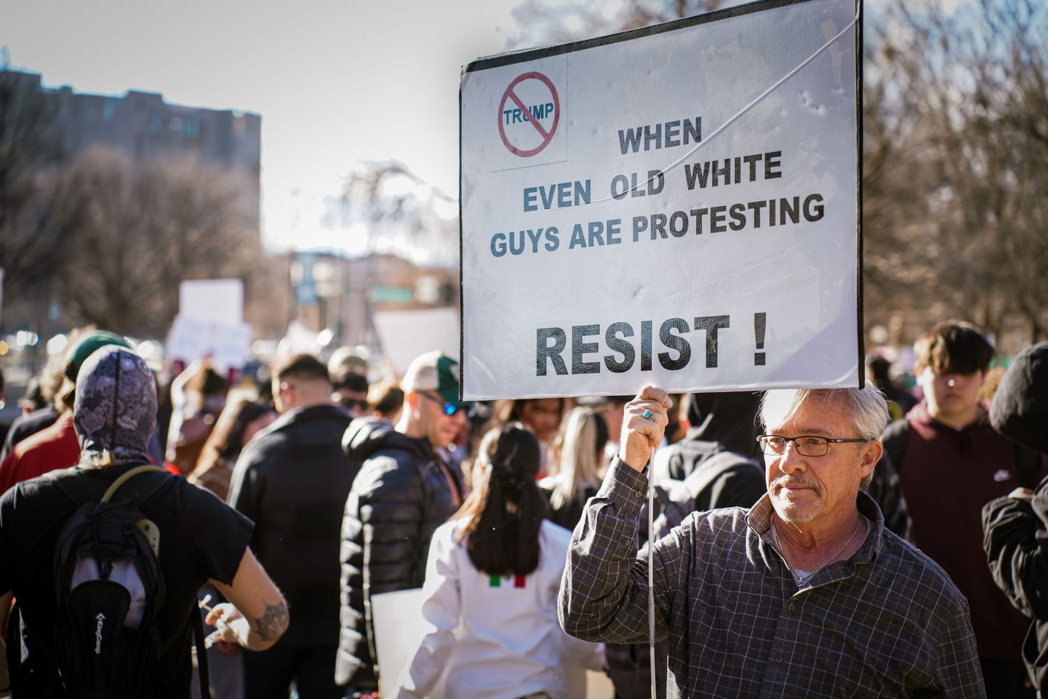 Older white man holding protest sign reading When Even Old White Guys Are Protesting Resist at a rally.
