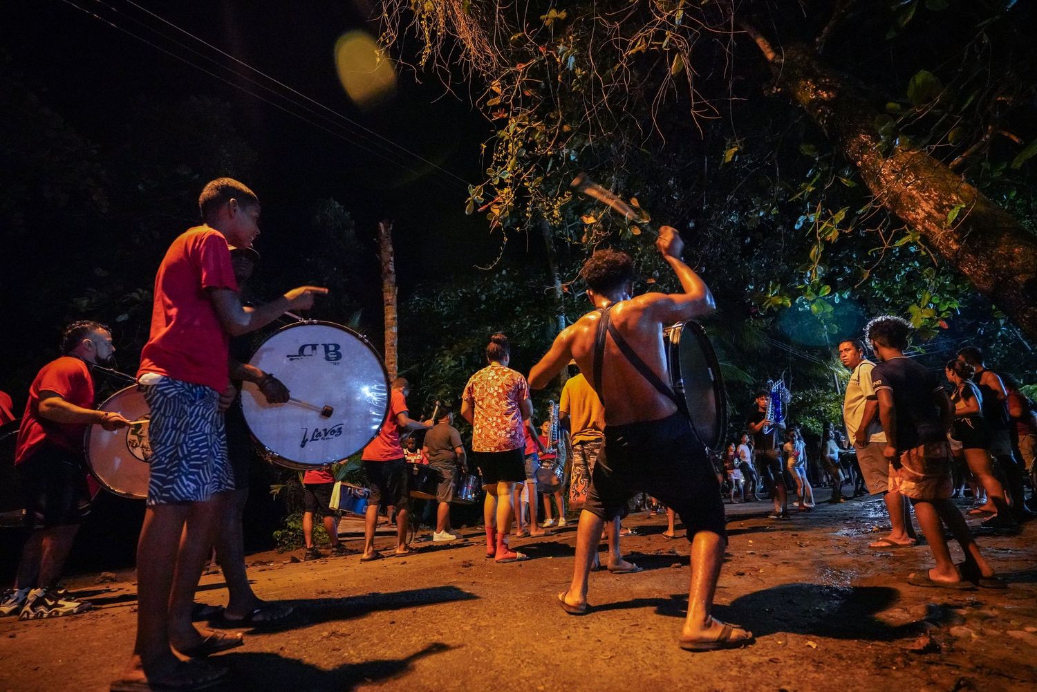 People playing drums and dancing outdoors at a lively nighttime street celebration.