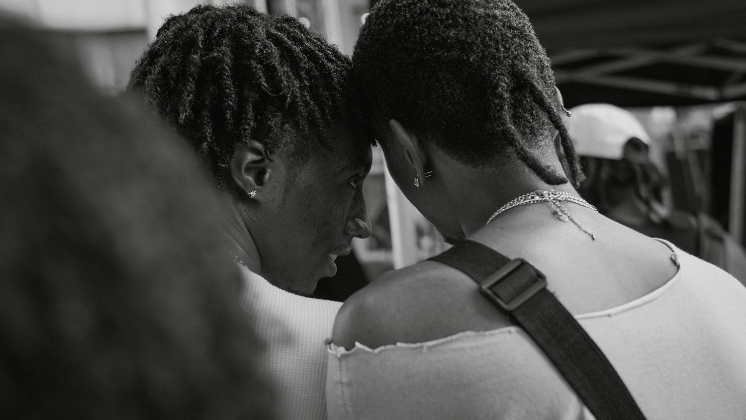 Two people with dreadlocks share an intimate moment, touching foreheads in a black and white street photography shot.