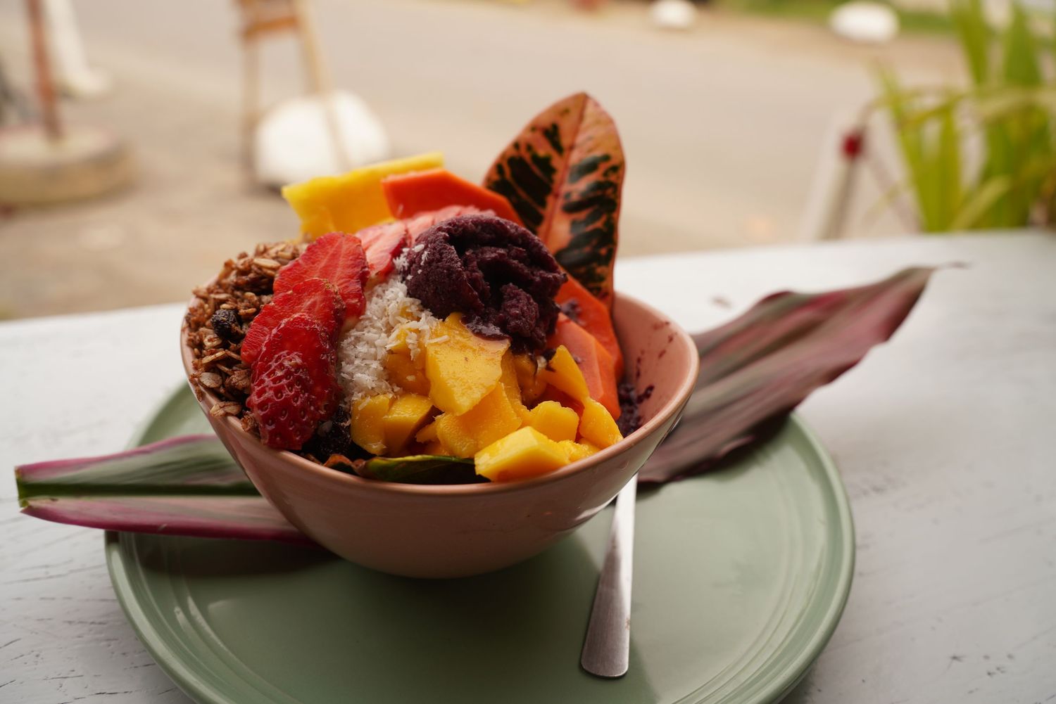 Colorful acai bowl topped with fresh mango, strawberries, granola, and tropical fruits served in a pink bowl.