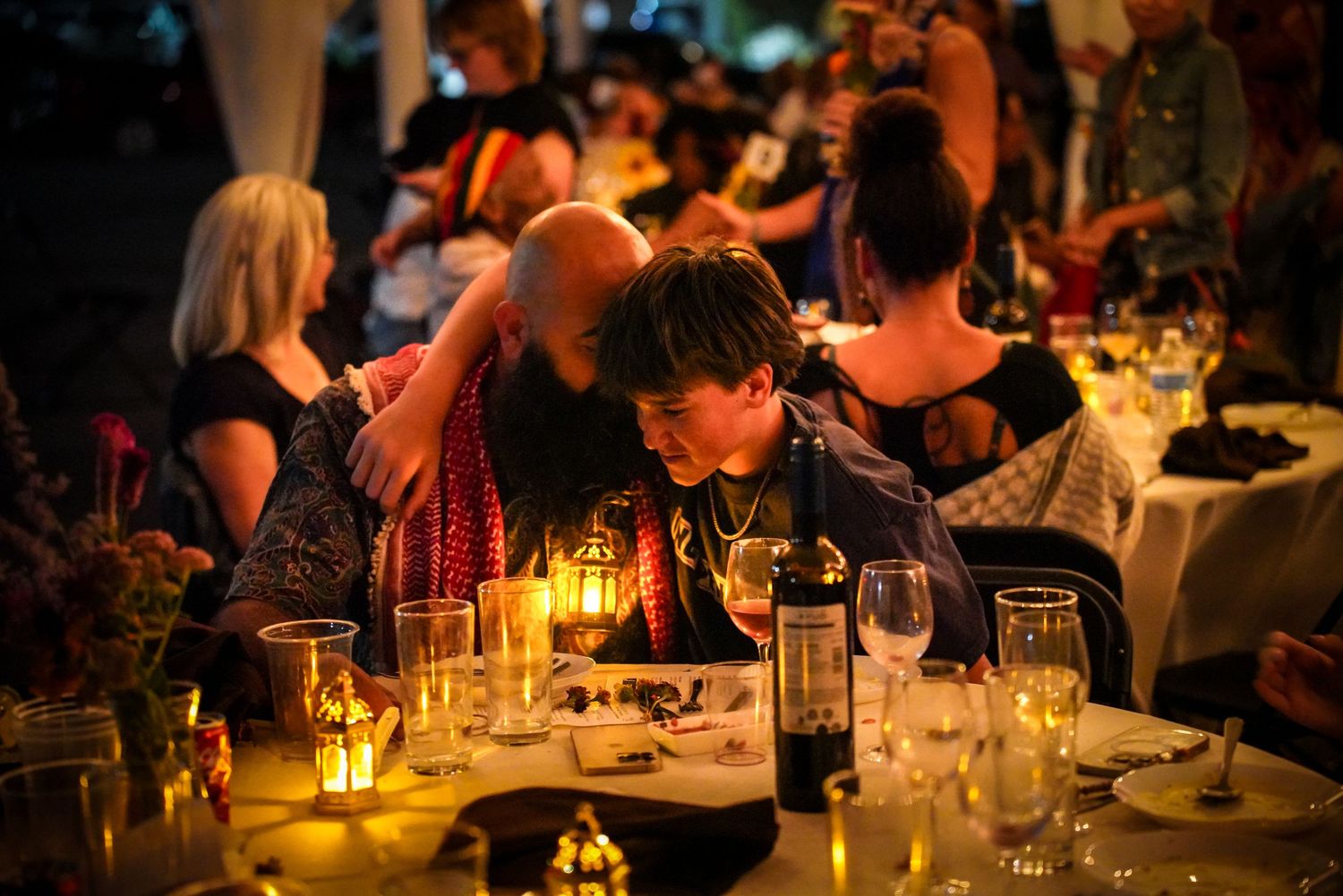 Two guests share an intimate moment at a candlelit outdoor dinner event with elegant table settings.