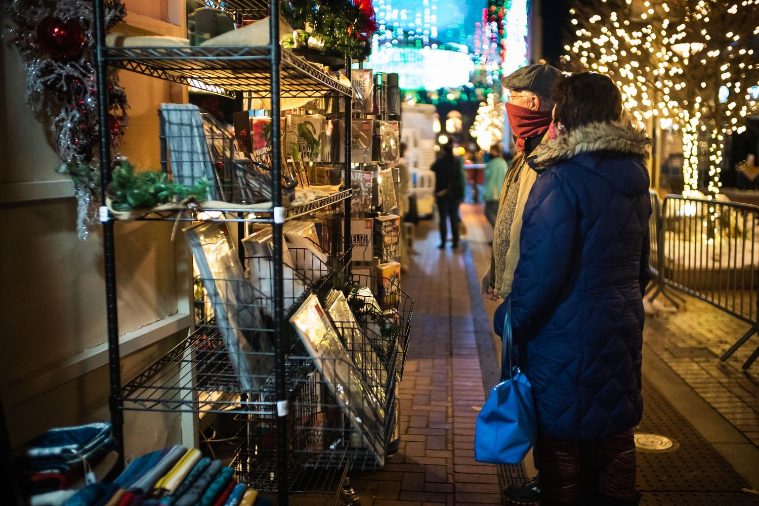 A woman in a blue puffer coat shopping at an outdoor Christmas market at night.