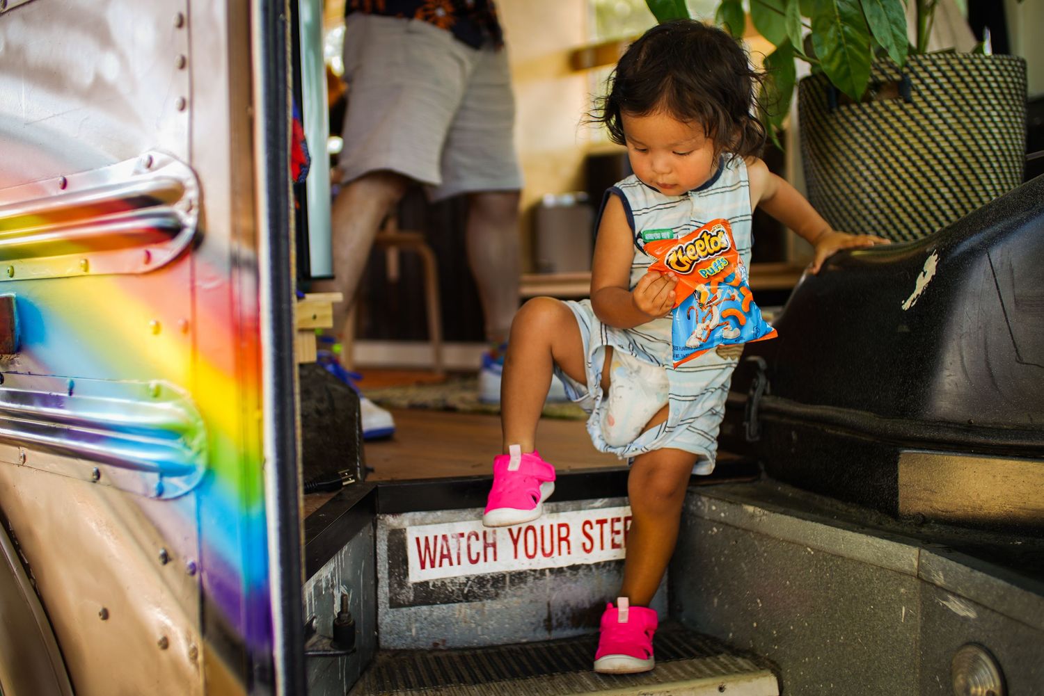 A young child in a striped dress stepping off a colorful bus marked Watch Your Step.