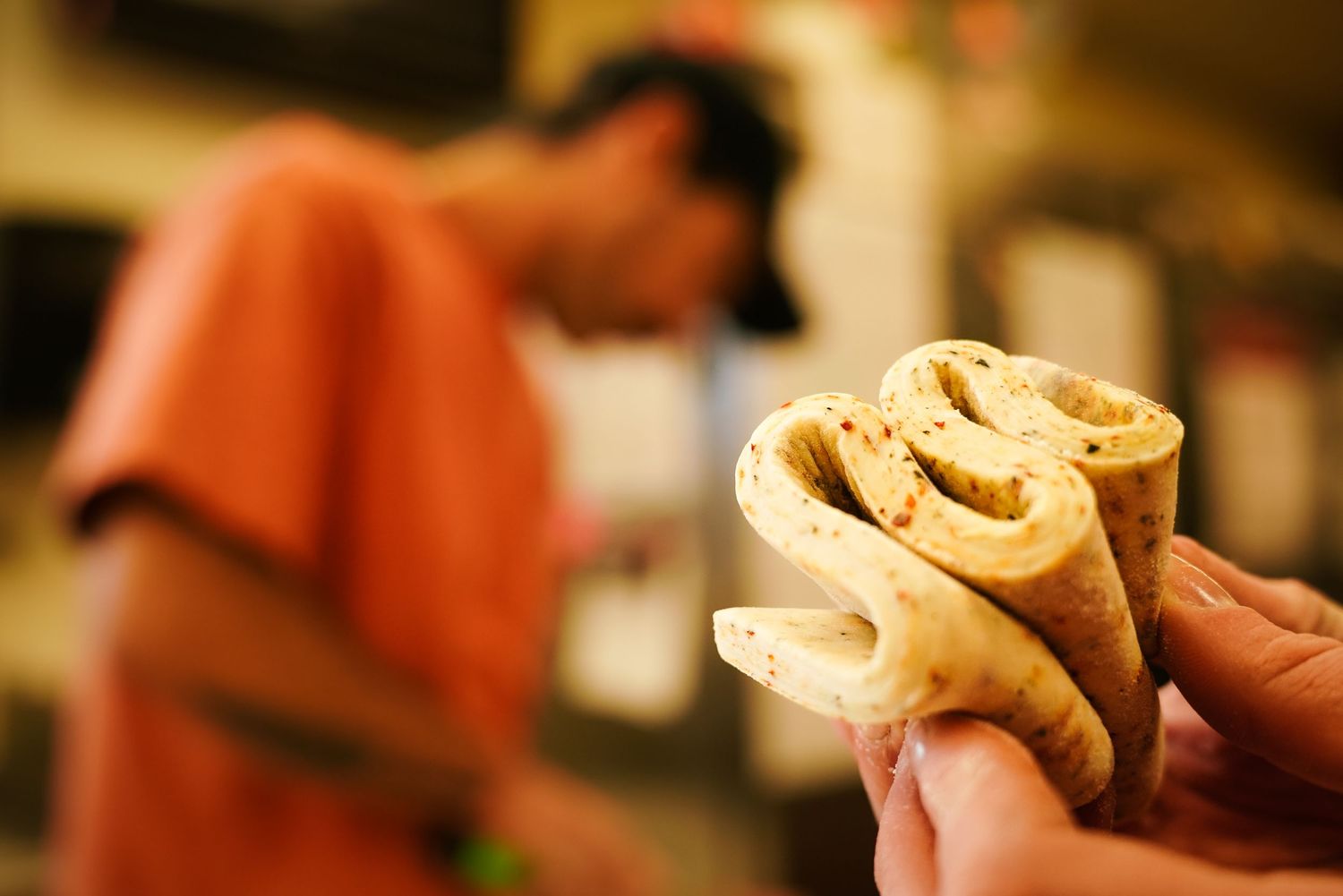 Close-up of hands holding rolled crepes with a vendor in an orange shirt in background.