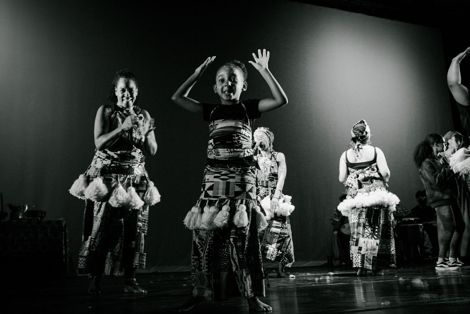 Black and white photo of African dancers performing energetically on stage in traditional costumes.