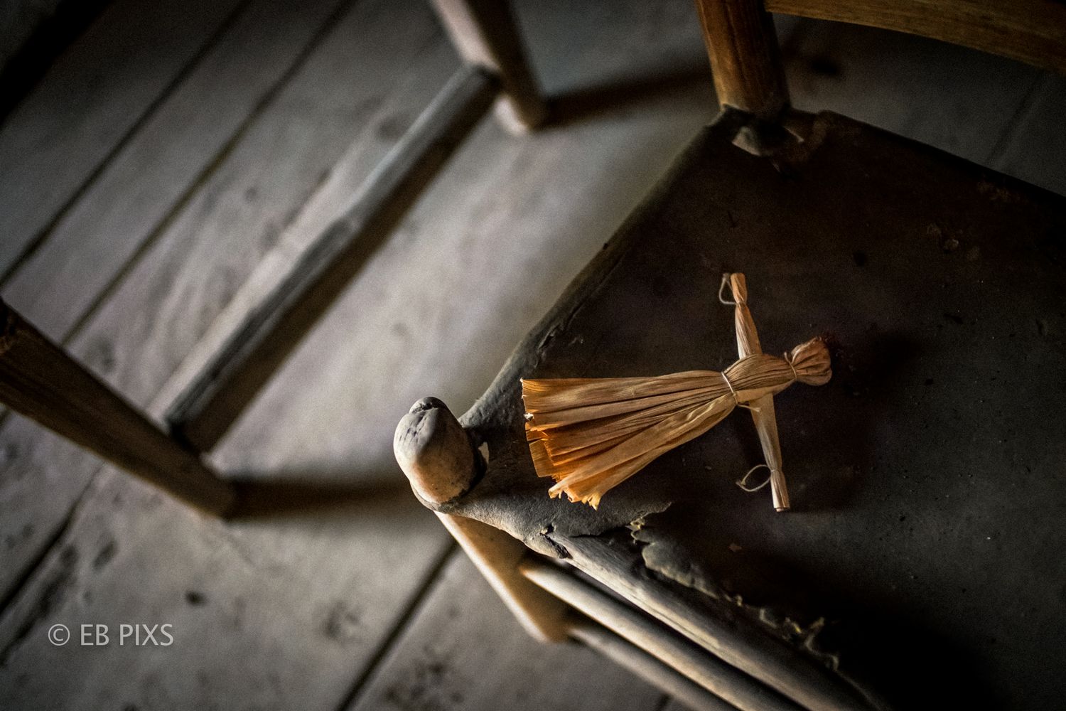 A rustic handmade straw doll resting on an old weathered wooden chair.