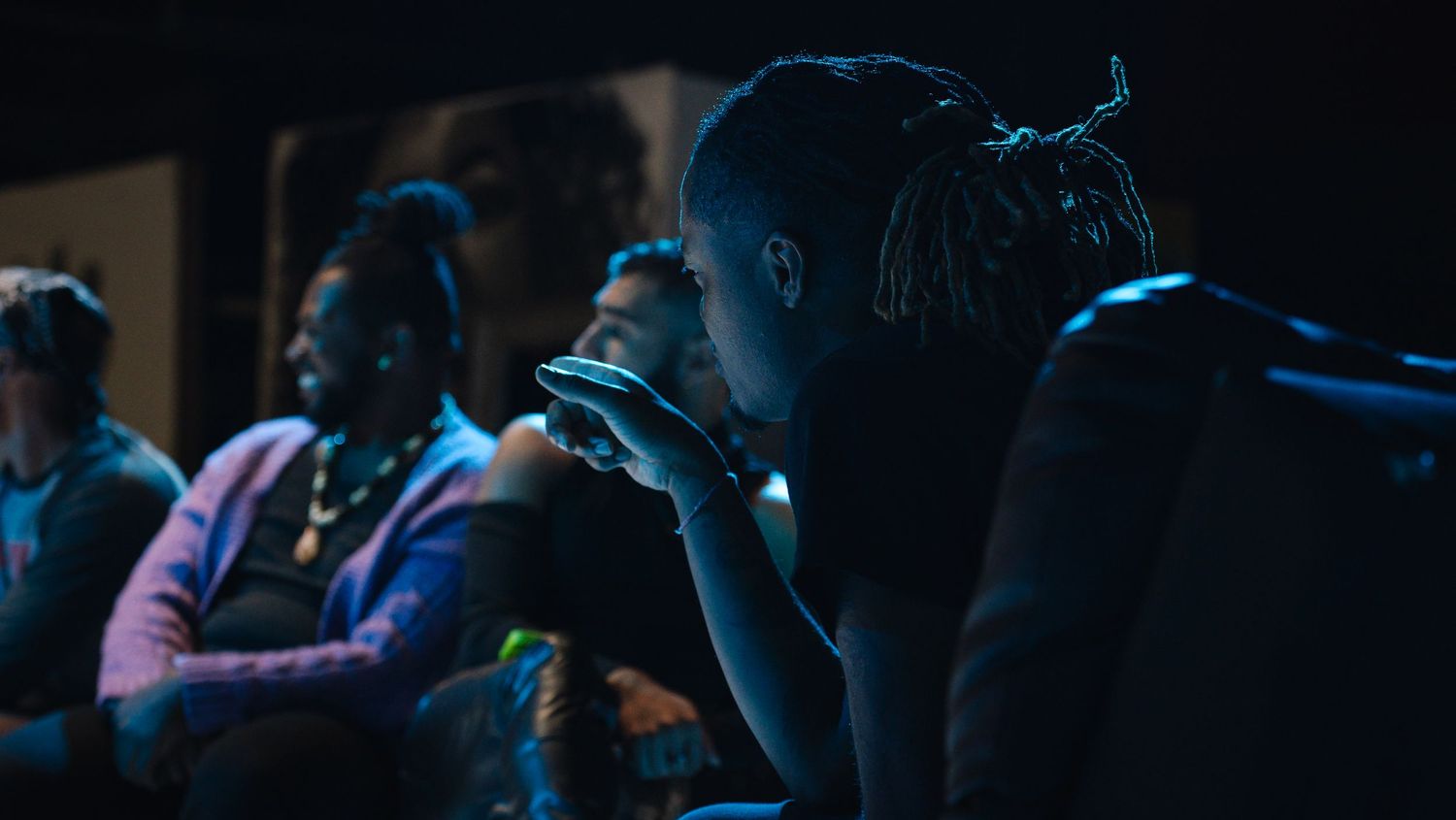 Person uses smartphone in dimly lit venue while audience members sit in background during event.