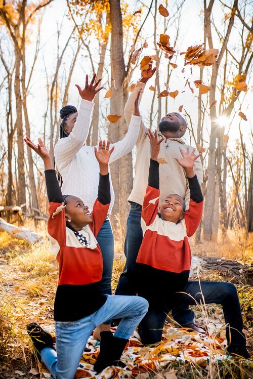 Happy family tosses autumn leaves in sunlit forest during fall outdoor photo session.