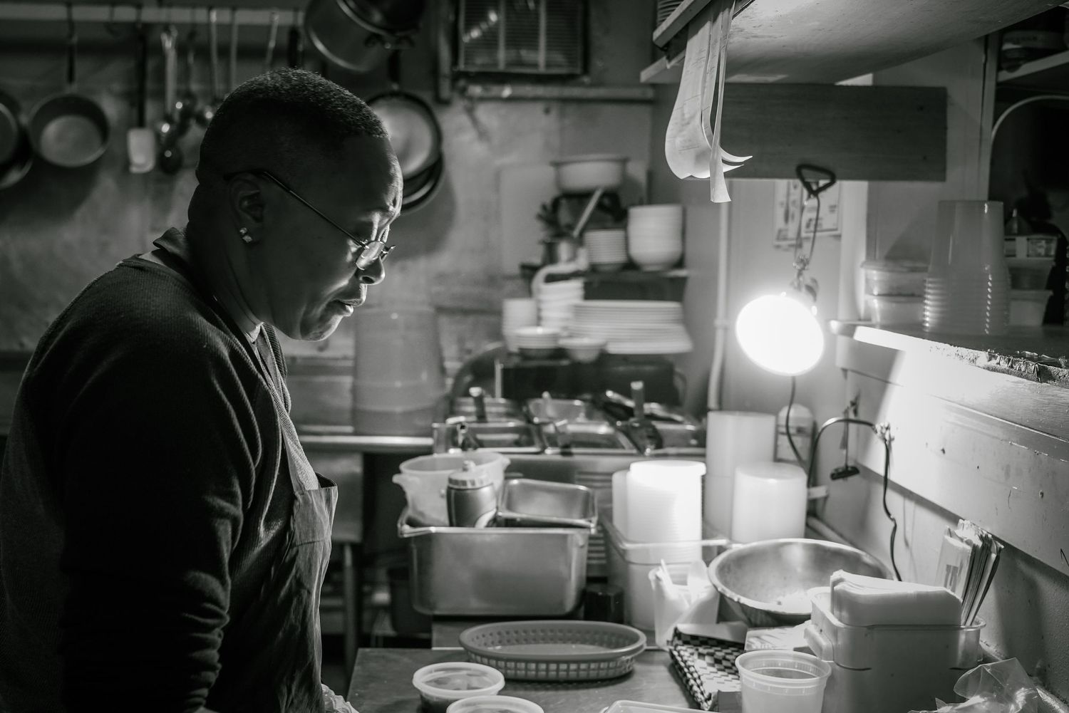 Black and white photo of a chef working in a busy restaurant kitchen surrounded by cookware and equipment.