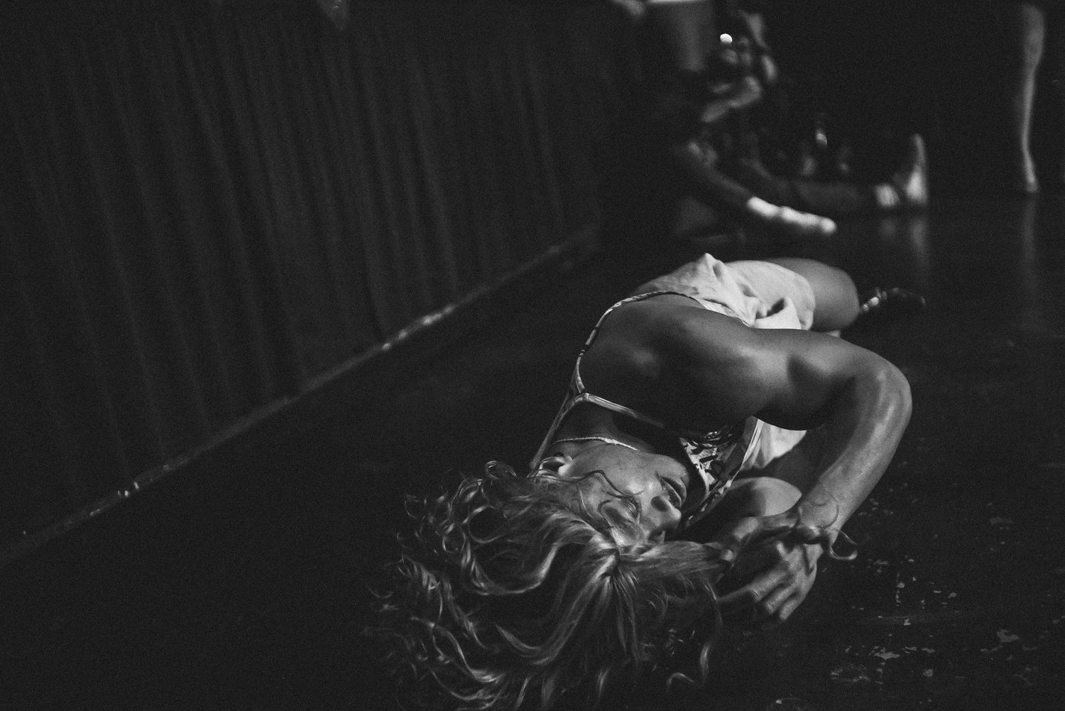 Black and white photo of performer lying on stage floor during dramatic dance performance.