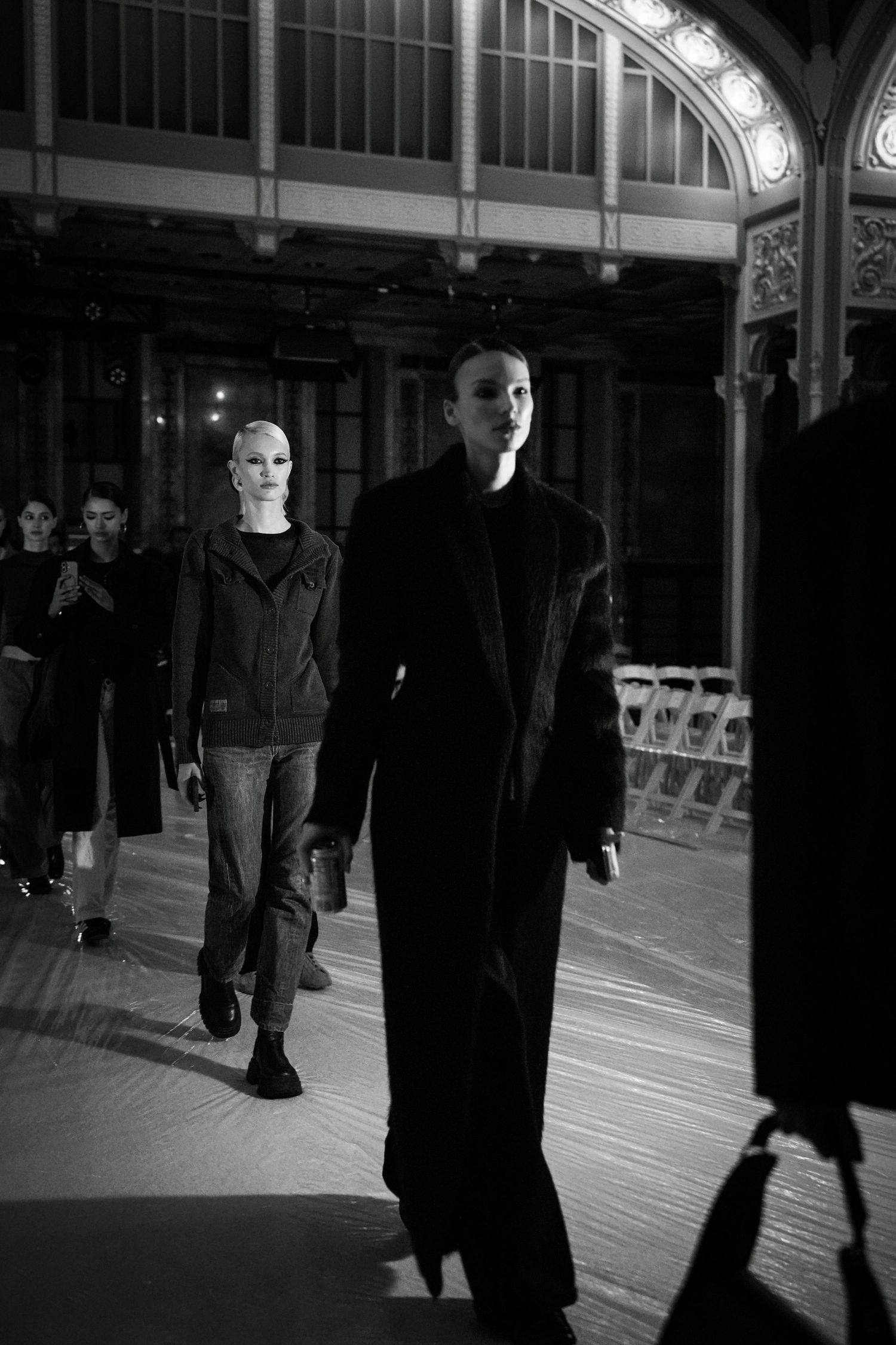 Fashion models walk runway in dark minimalist clothing during black and white fashion show.